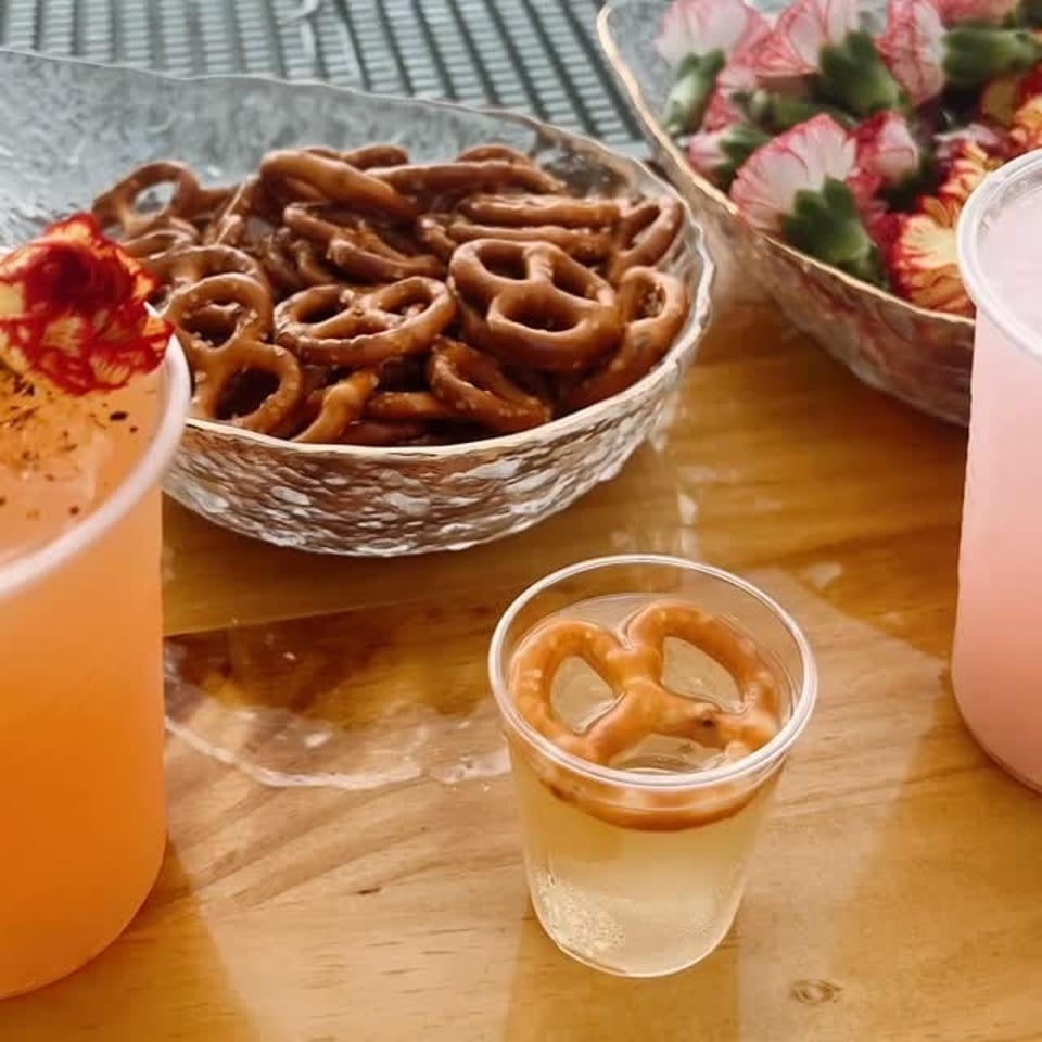 A wooden table with bowls of pretzels, strawberries, and various drinks.