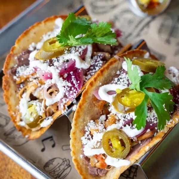 Two crispy tacos filled with meat, beans, cheese, pickled onions, jalapeños, and cilantro.