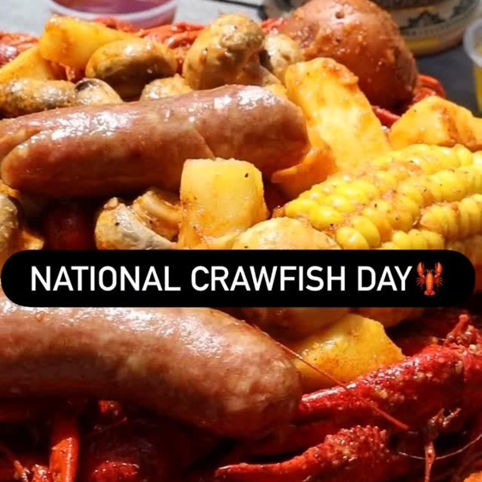 A close-up of a crawfish boil with sausage, corn, potatoes, and mushrooms, with a beer stein in the background.