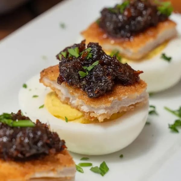 Three deviled eggs topped with fried chicken and dark relish, garnished with parsley on a white plate.