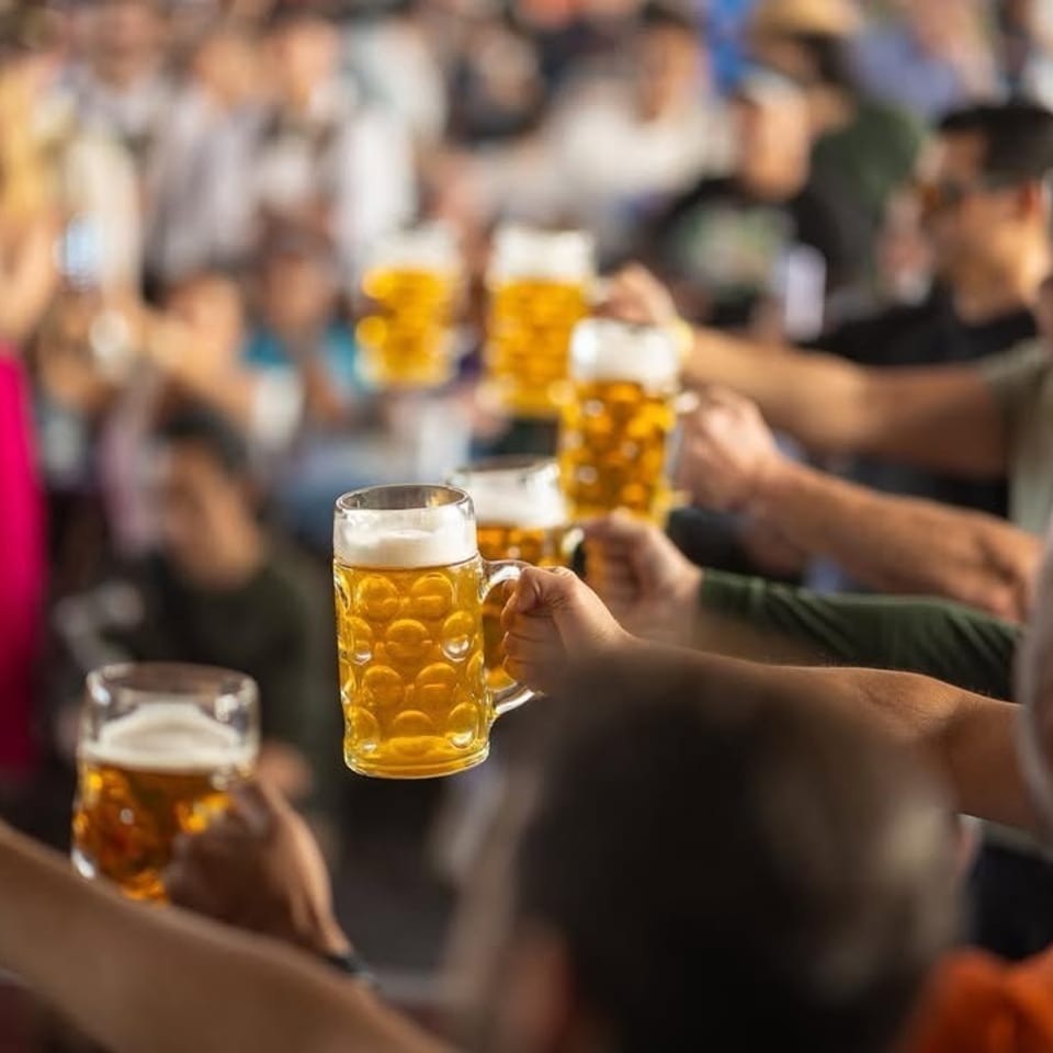 People holding up beer steins in a crowded, festive atmosphere.