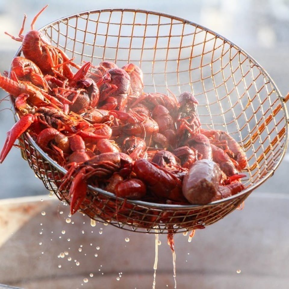 Steaming red crawfish and sausage being lifted from a pot in a metal basket.