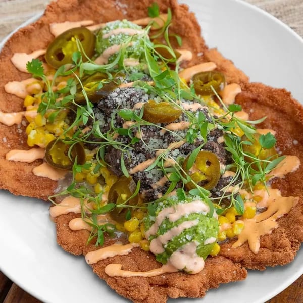 Crispy fried chicken schnitzel topped with black beans, corn, jalapeños, guacamole, and sauce.