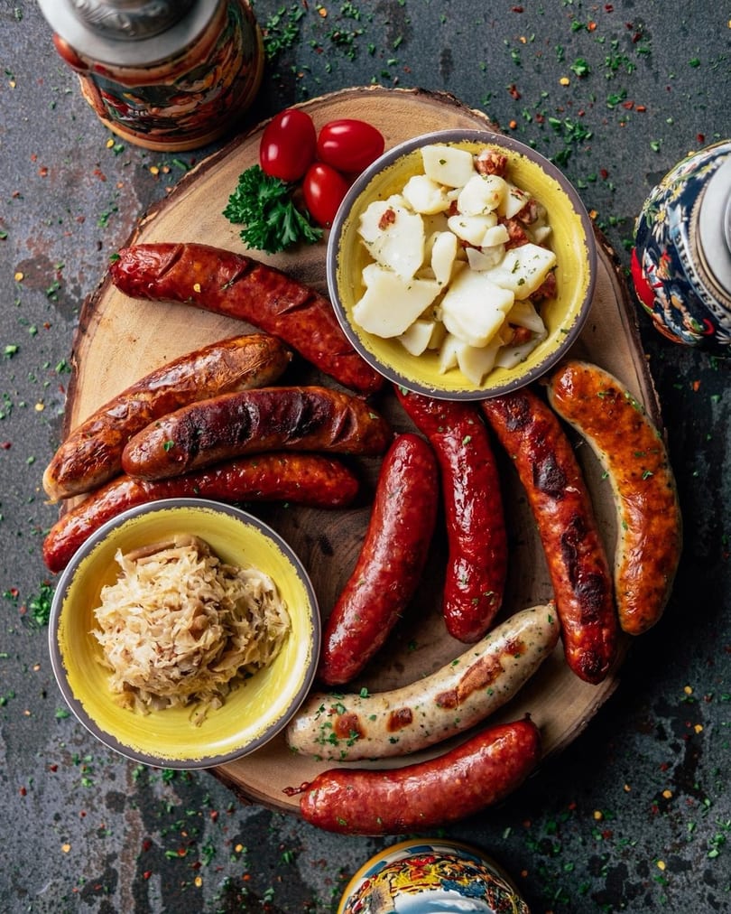 Assorted grilled sausages with sauerkraut and potato salad on a wooden board.