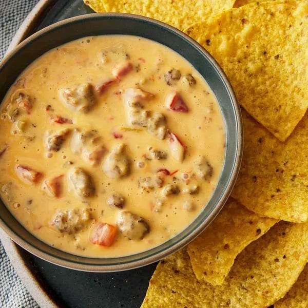 A bowl of creamy queso dip with ground meat and diced tomatoes, served with tortilla chips.